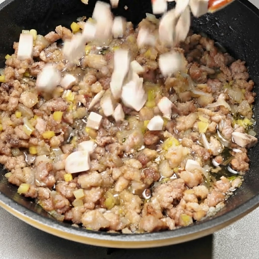 Diced mushrooms being tossed into the pan with the seasoned pork mixture.