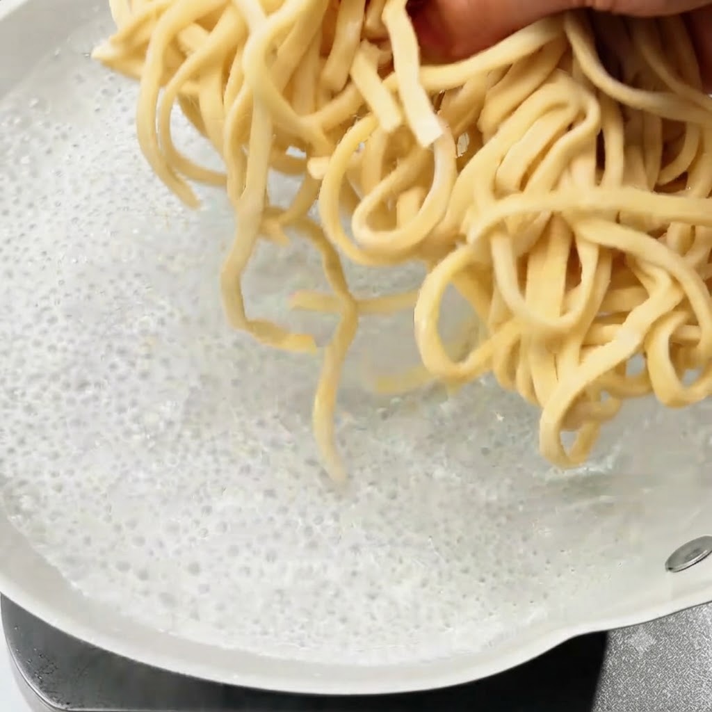Fresh noodles being dropped into a pot of boiling water.