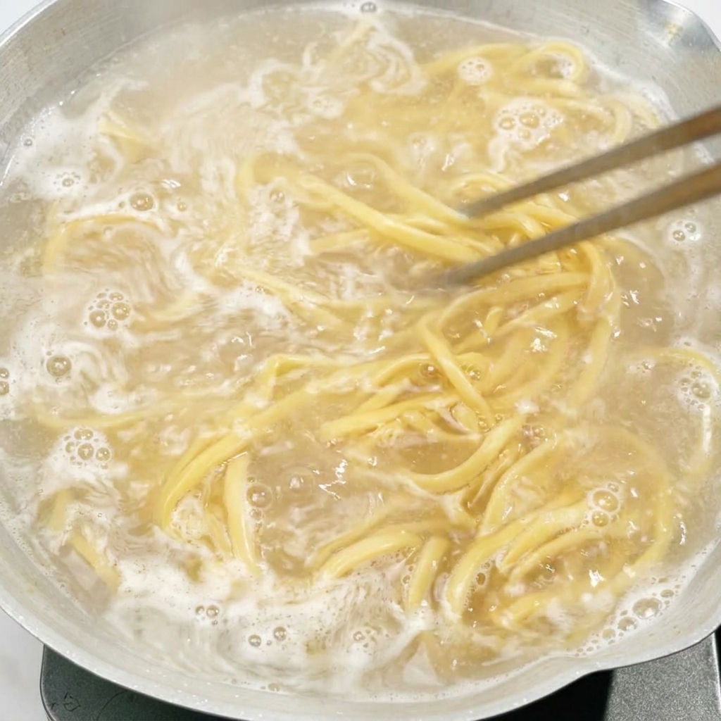 Chopsticks stirring noodles boiling in a pot of water.