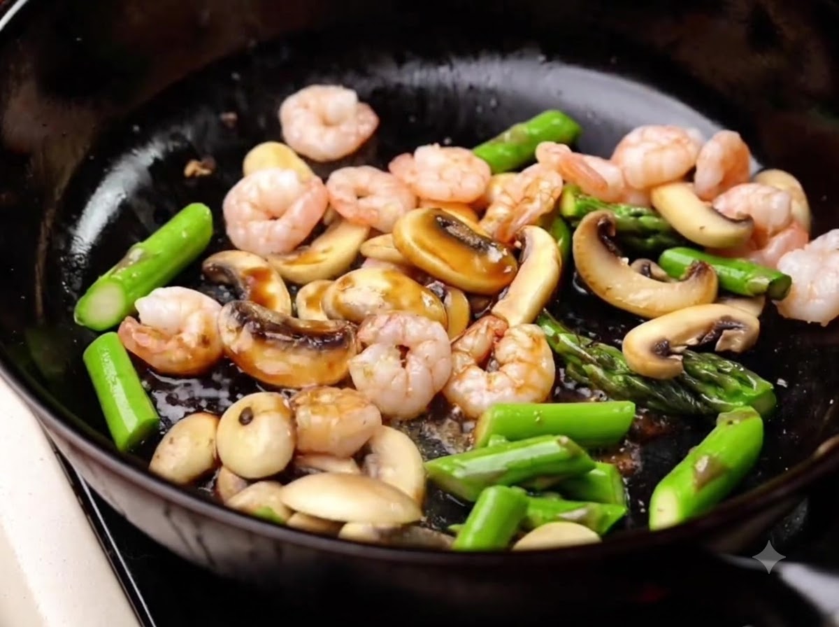 Light soy sauce being poured into the pan over the shrimp, asparagus, and mushrooms, and stirred together.