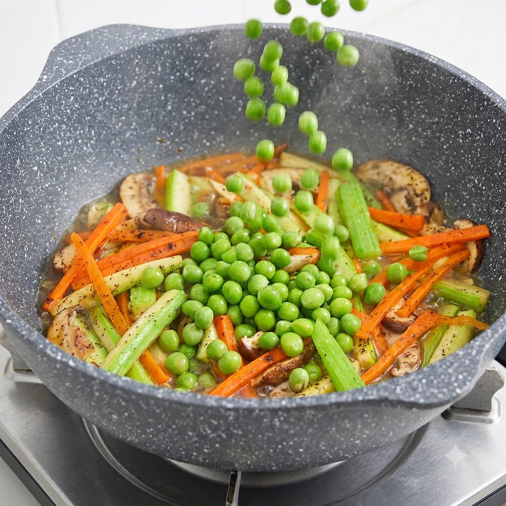 Green peas falling from above into a pan filled with sliced mushrooms, carrots, and zucchini.