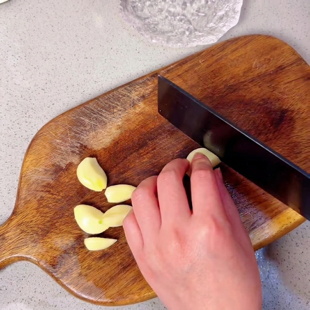 Garlic cloves arranged on a wooden chopping board ready to be minced.
