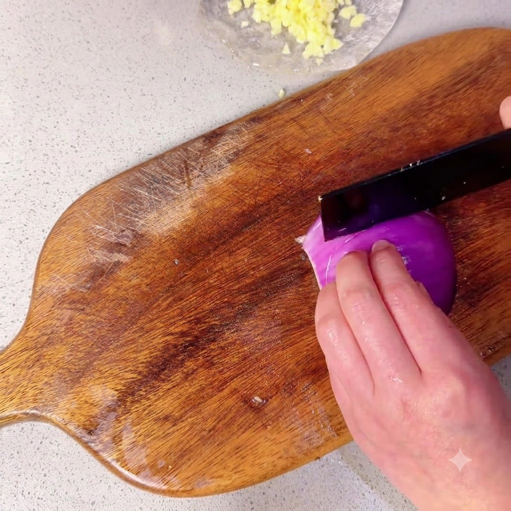 Half of a red onion being sliced into small pieces on a wooden cutting board.
