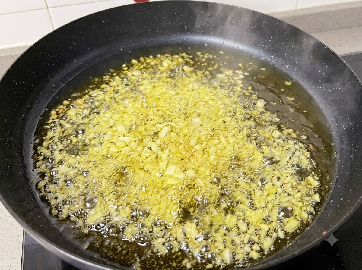 Minced garlic and onions frying and bubbling in hot oil inside a black pan.