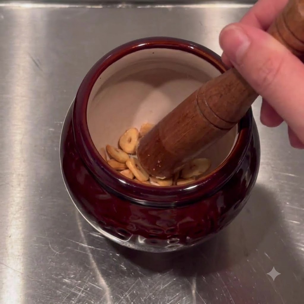 Fried garlic chips in various shades being placed inside a dark red ceramic mortar bowl.