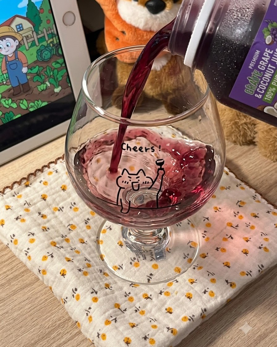 Dark purple grape juice being poured from a carton into a clear stemmed glass featuring a cartoon cat design.
