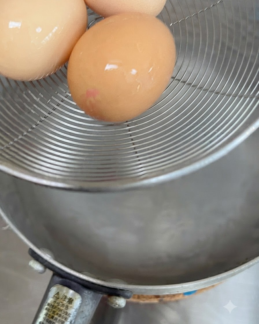 Three raw eggs resting in a wire strainer basket held above hot water.