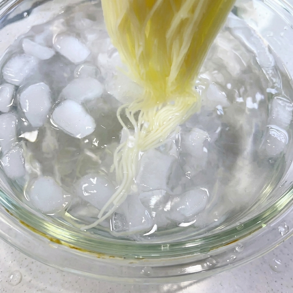 Chopsticks stirring cooked noodles in an ice-water bath filled with ice cubes.