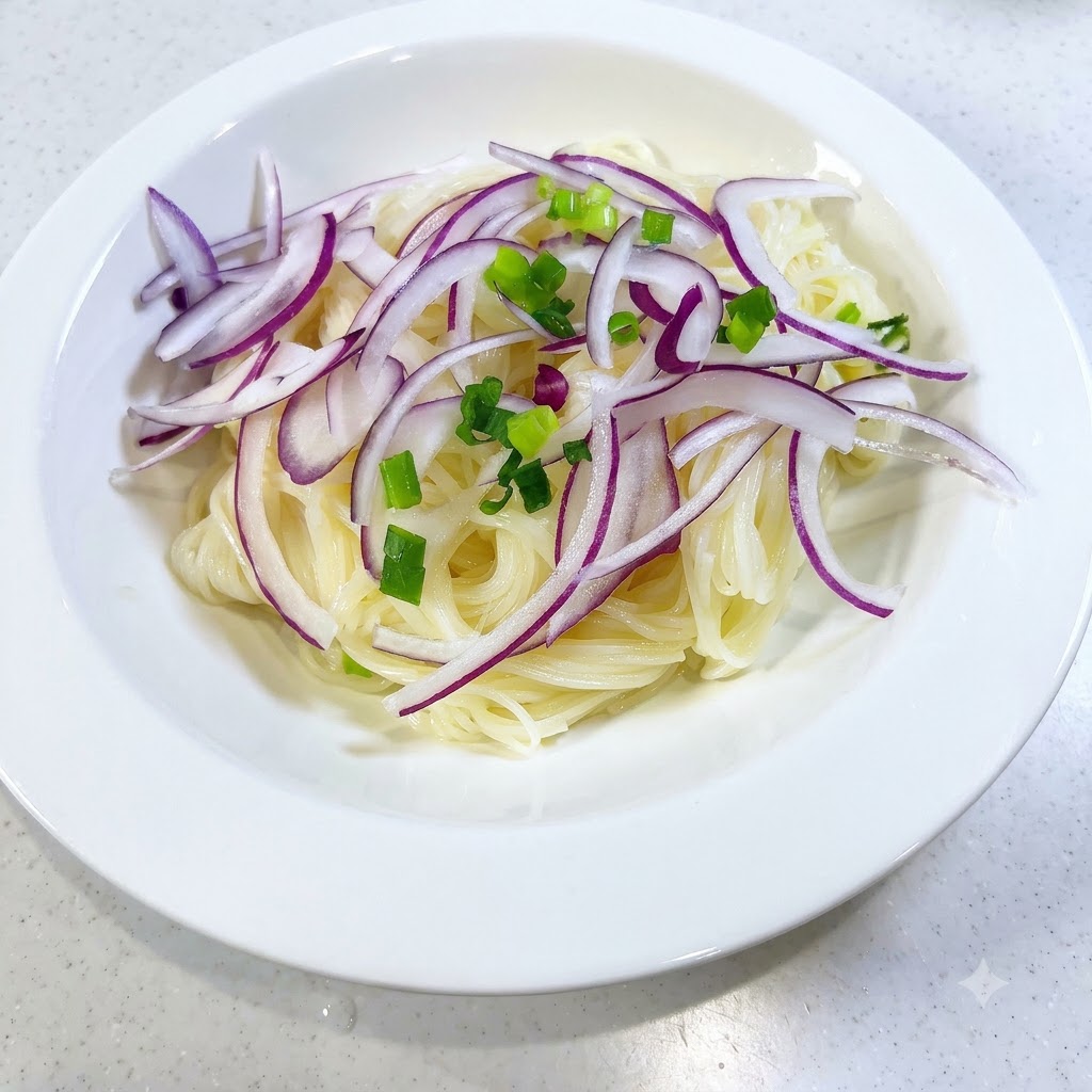 Freshly chopped green onions scattered across noodles and red onion slices in a white bowl.