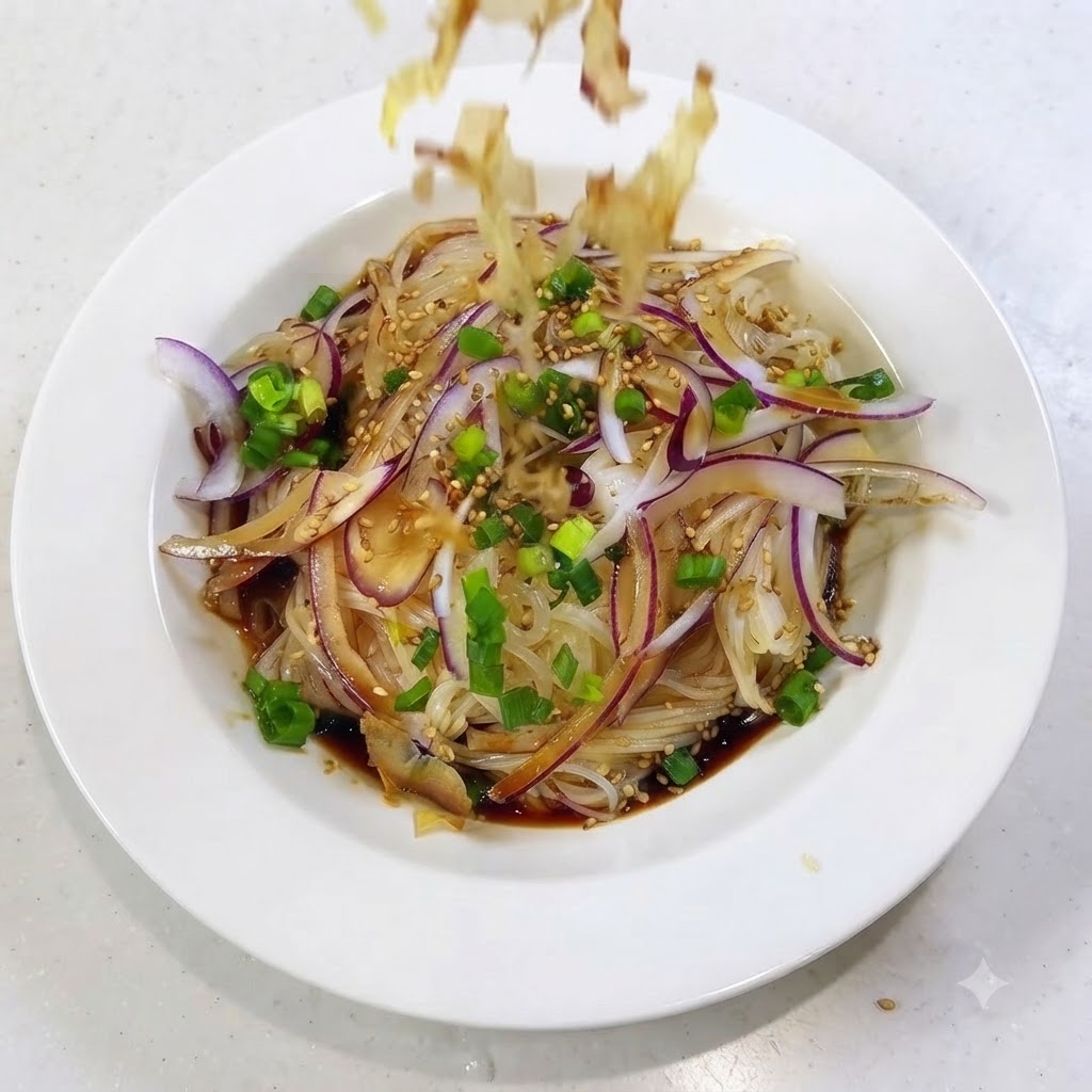 Bonito flakes falling and scattering over the top of the prepared noodle dish.