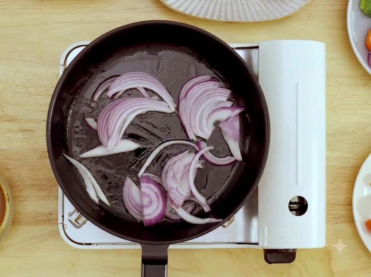 Sliced red onions being stir-fried in a hot pan with a wooden spatula.
