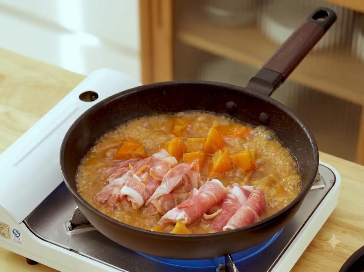 Raw rolled beef slices arranged inside a frying pan with bubbling brown miso broth and carrot pieces.