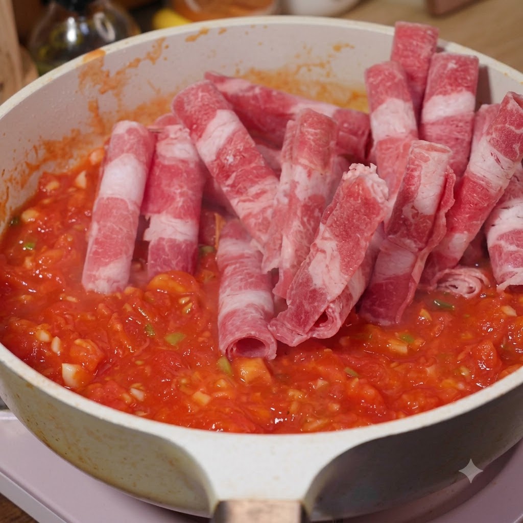 Sliced fatty beef being added into a pan with tomatoes and stir-fried.