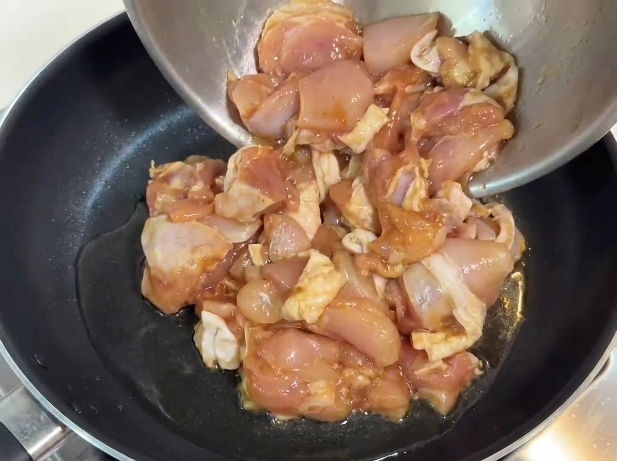 Marinated chicken pieces being poured into a pan with hot oil.
