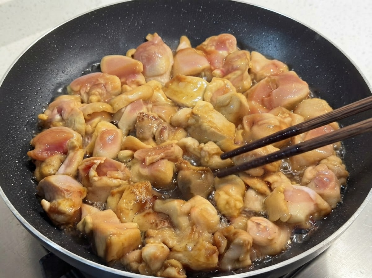 Marinated chicken pieces being pan-fried in a skillet and carefully flipped using wooden chopsticks.