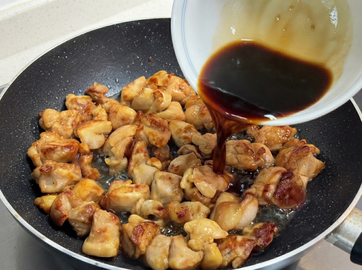 A dark, savory sauce mixture being poured from a white bowl over golden-brown pan-fried chicken pieces in a skillet.