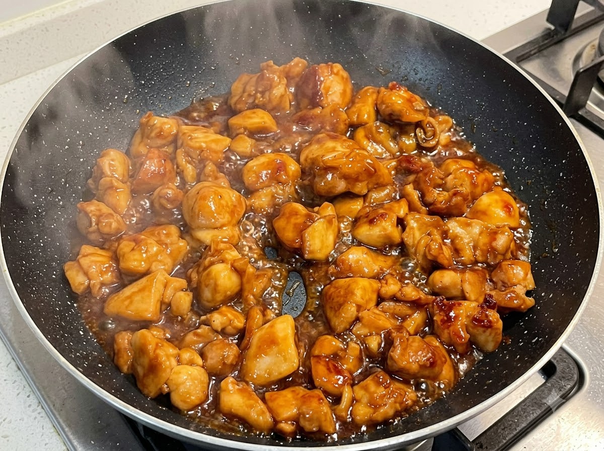 Chicken simmering in thick sauce inside a frying pan.