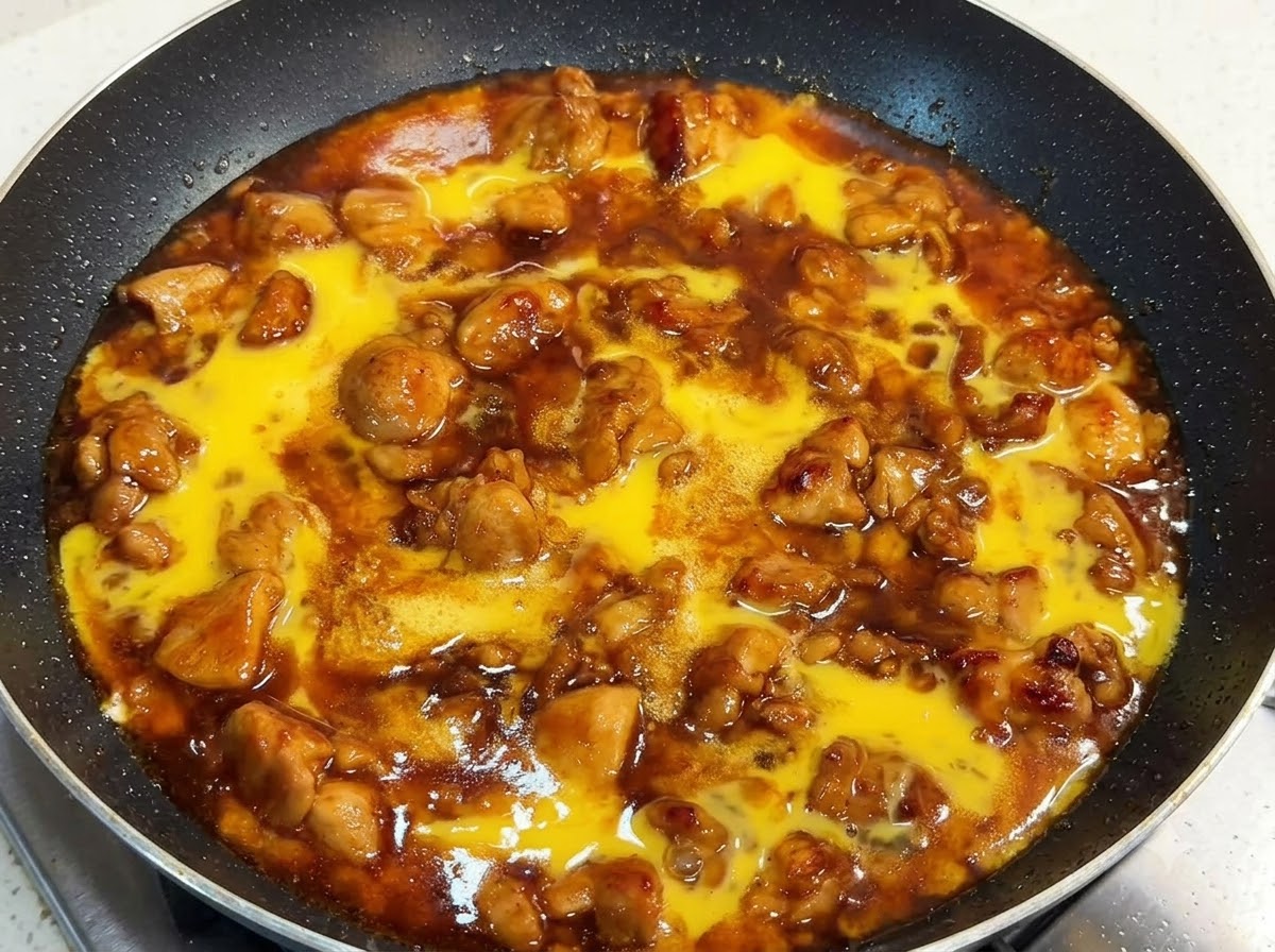 A pan filled with chicken pieces and rich sauce topped with raw beaten egg liquid, covered with a lid.