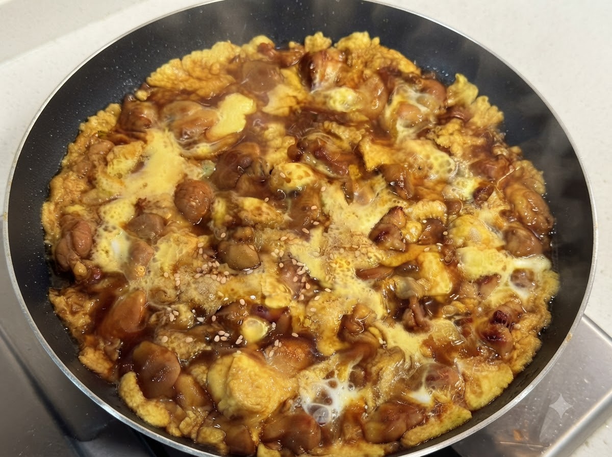 A hot skillet filled with tender cooked chicken and silky egg in a savory dark sauce, garnished with white sesame seeds.