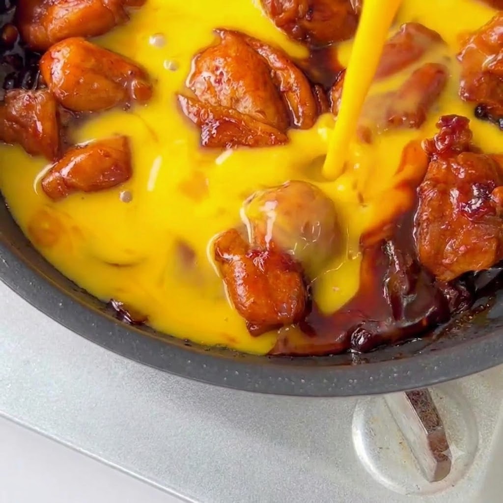 Chicken and egg mixture garnished with sesame seeds and green onions in a pan.