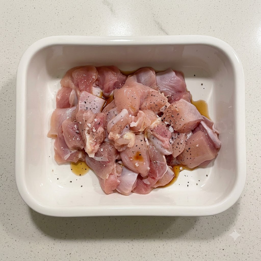 Raw chicken pieces seasoned with starch, soy sauce, and black pepper inside a white ceramic container.