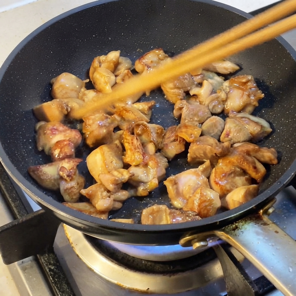 Chicken pieces being stir-fried in a pan with chopstickscite: 1.