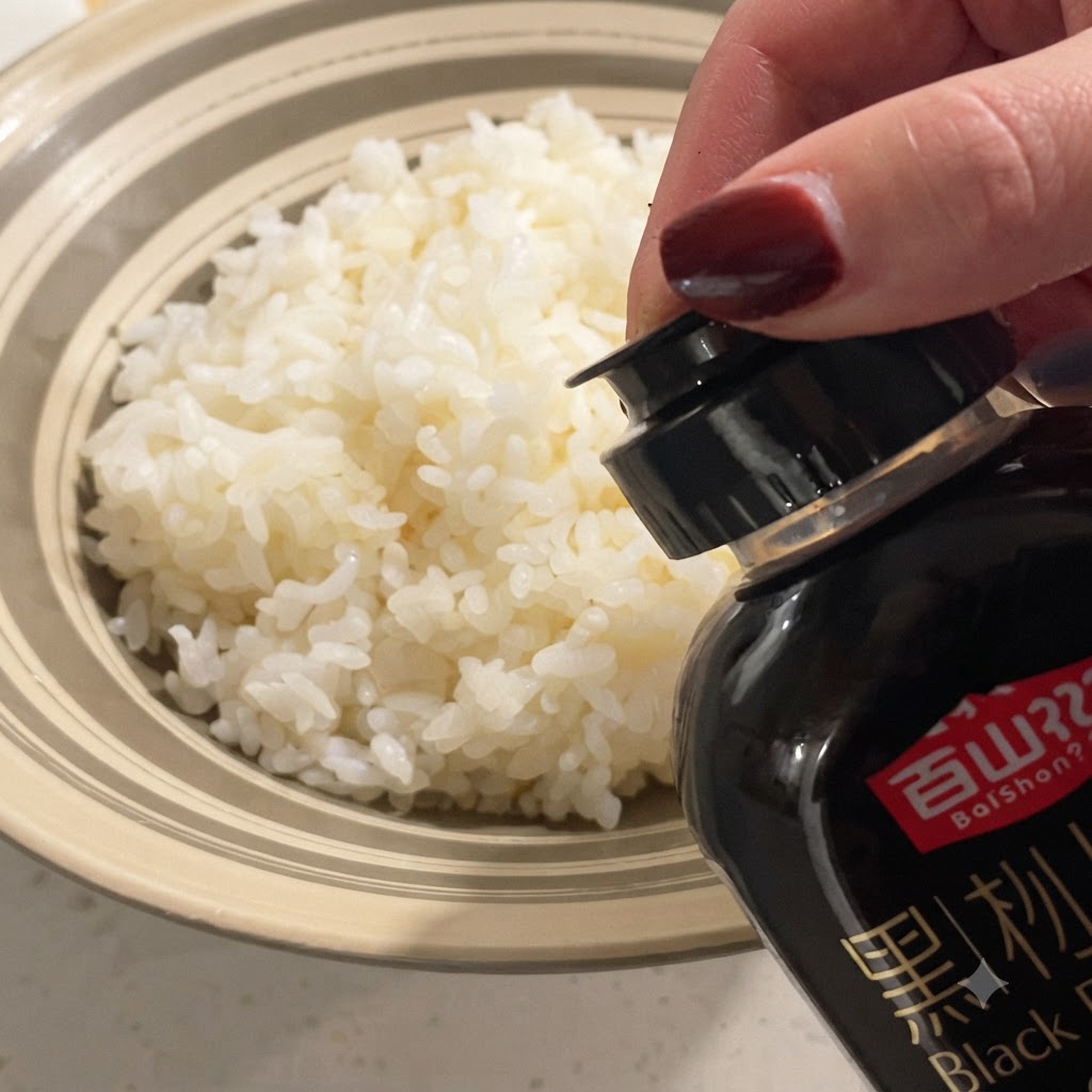 Black truffle sauce being drizzled from a bottle onto a bowl of fluffy steamed white rice.