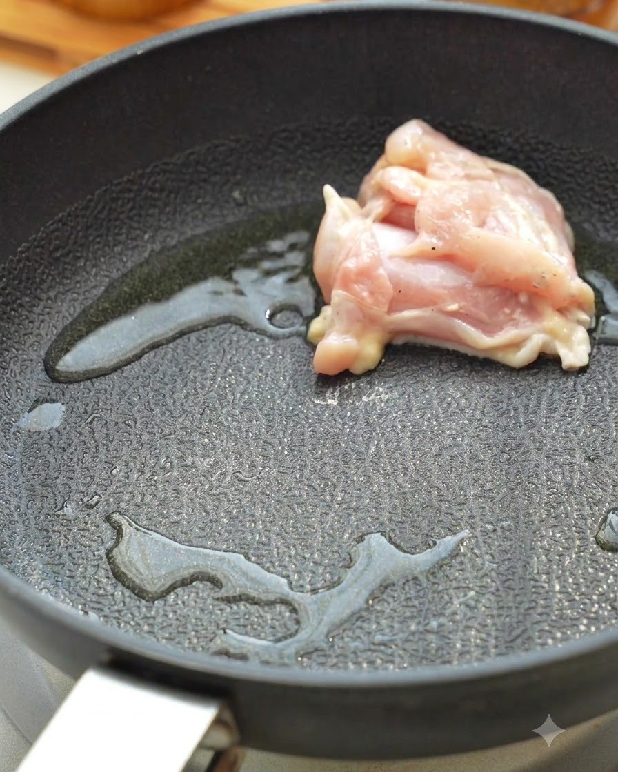 Raw chicken thigh pieces searing in a hot skillet with oil.