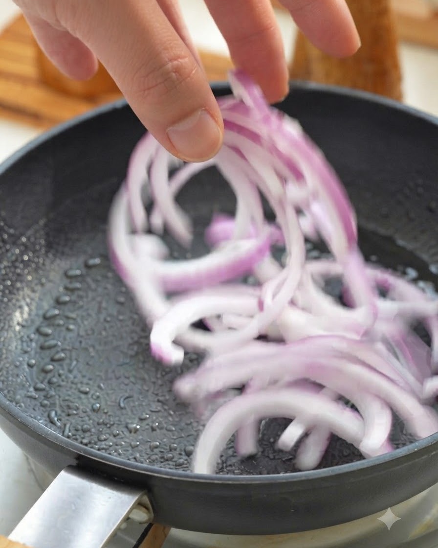 Sliced red onions being tossed into a hot frying pan.