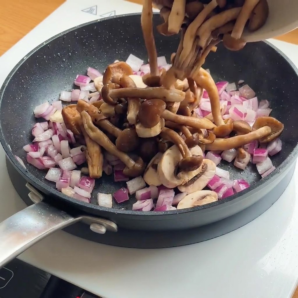 Sliced mushrooms and red onions being added to a frying pan with already browned chicken pieces.