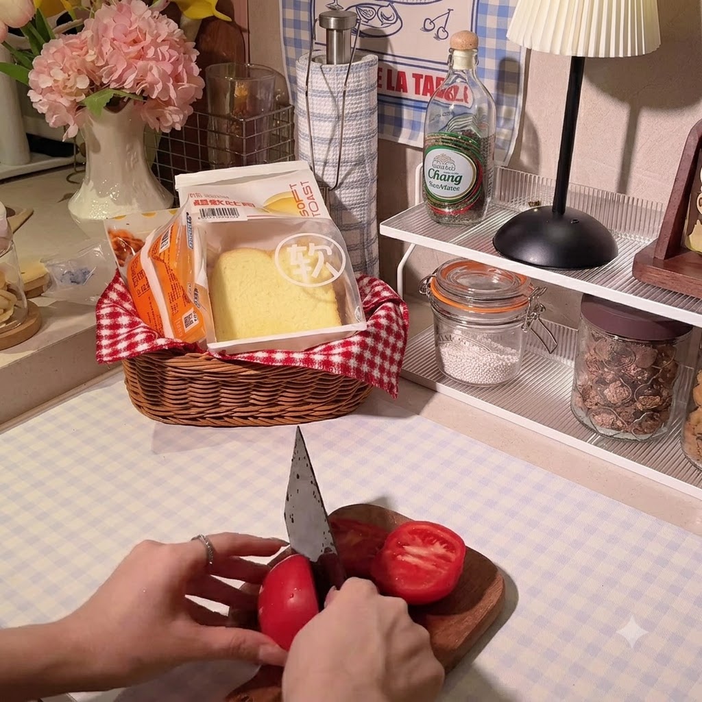 A persons hands using a chefs knife to slice a bright red tomato on a wooden cutting board.