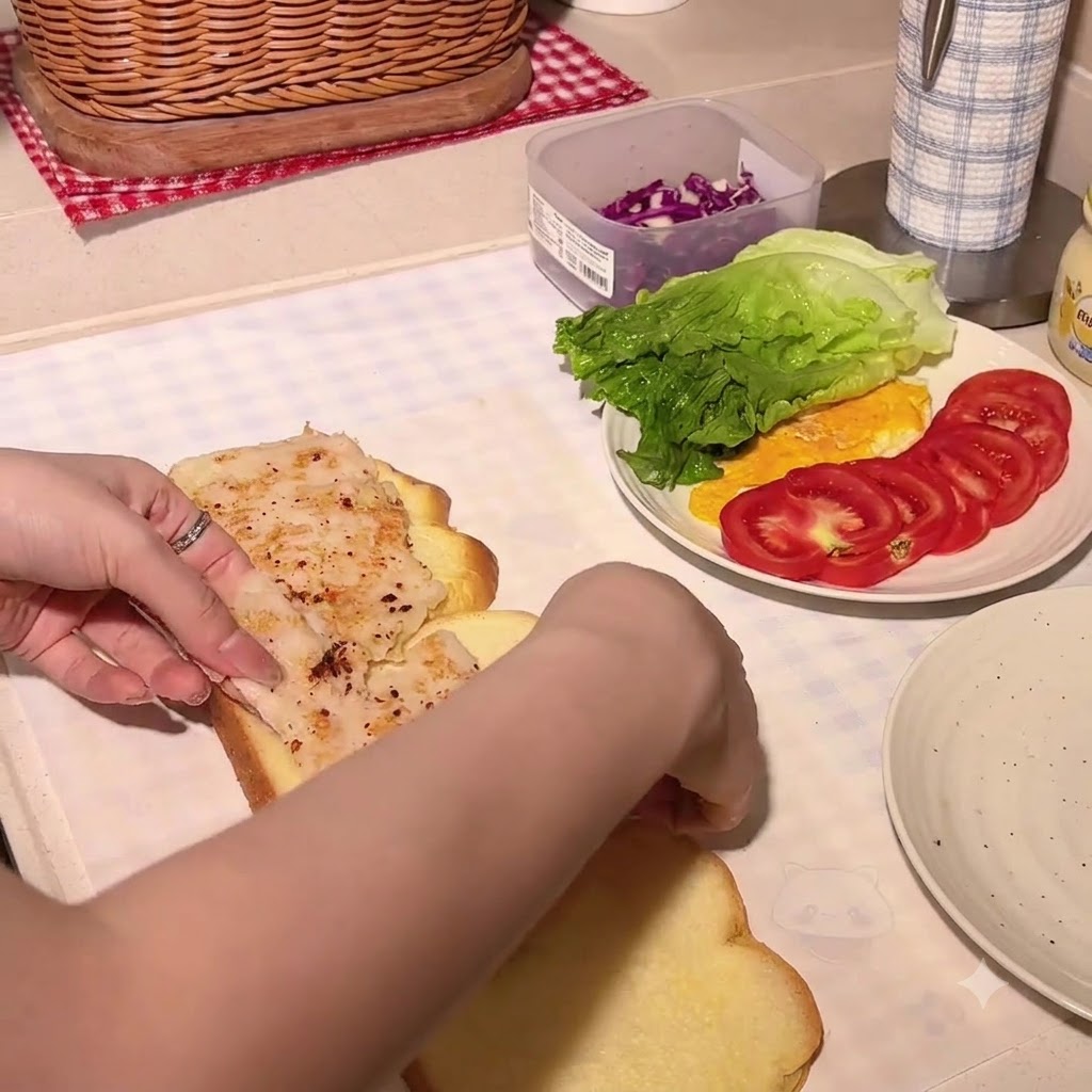 Honey mustard being squeezed onto a pumpkin bread slice with a chicken cutlet.