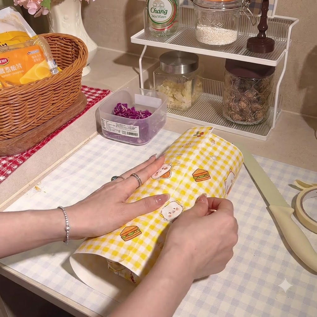 The thick sandwich being wrapped securely inside checkered parchment paper.