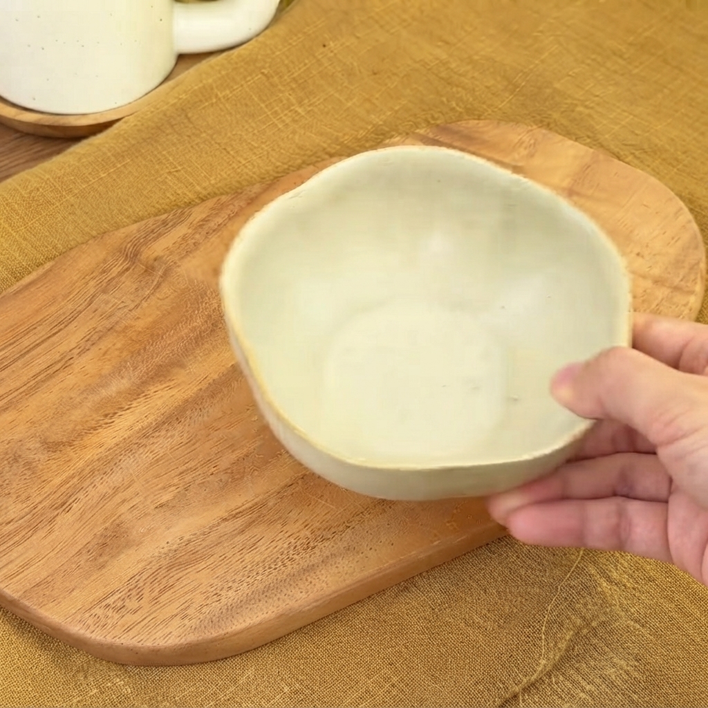 A small empty ceramic bowl held over a wooden board ready for sauce mixing.
