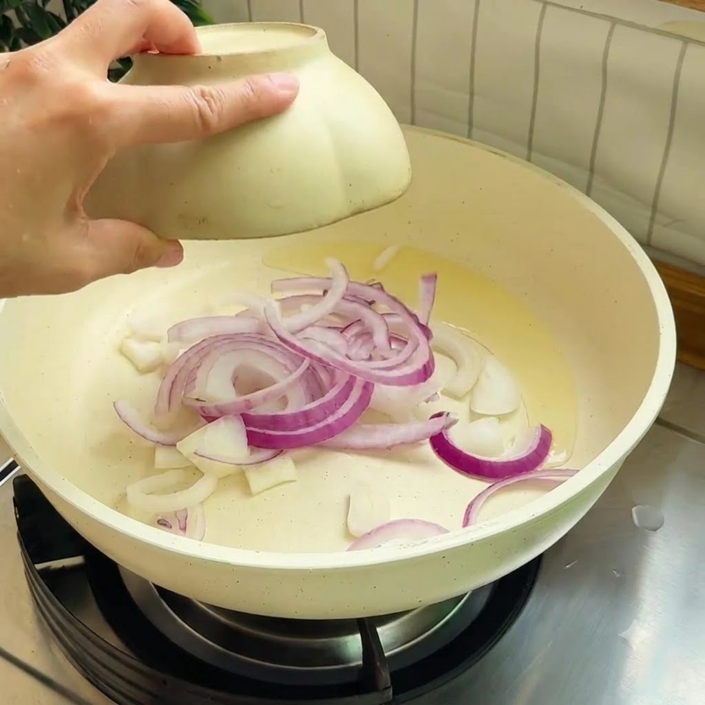 Red onion strips sautéing in a hot pan with cooking oil.