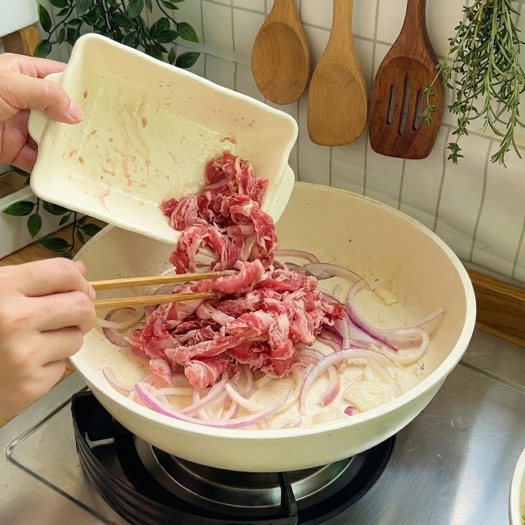 Raw beef slices being added to the pan with onions for stir-frying.