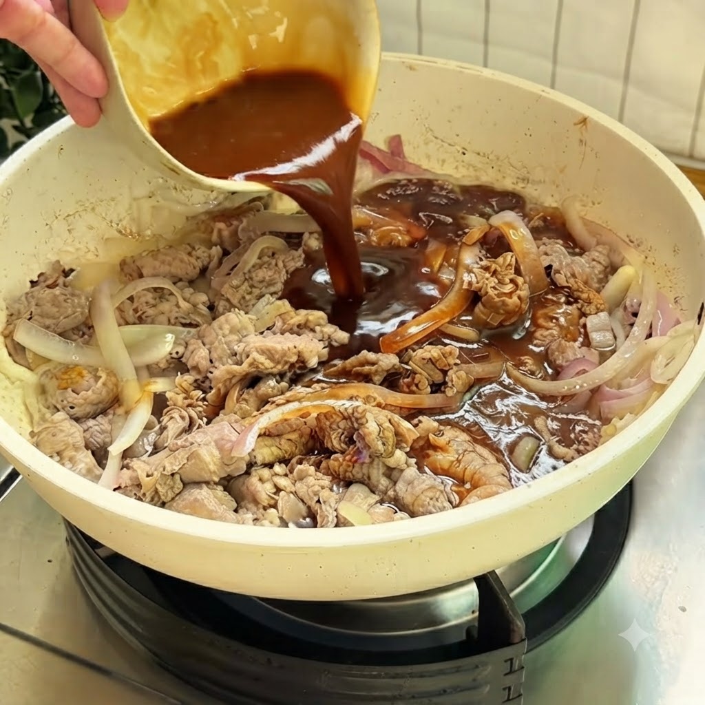 Rich brown sauce being poured from a small bowl into a white skillet containing beef and sliced onions.