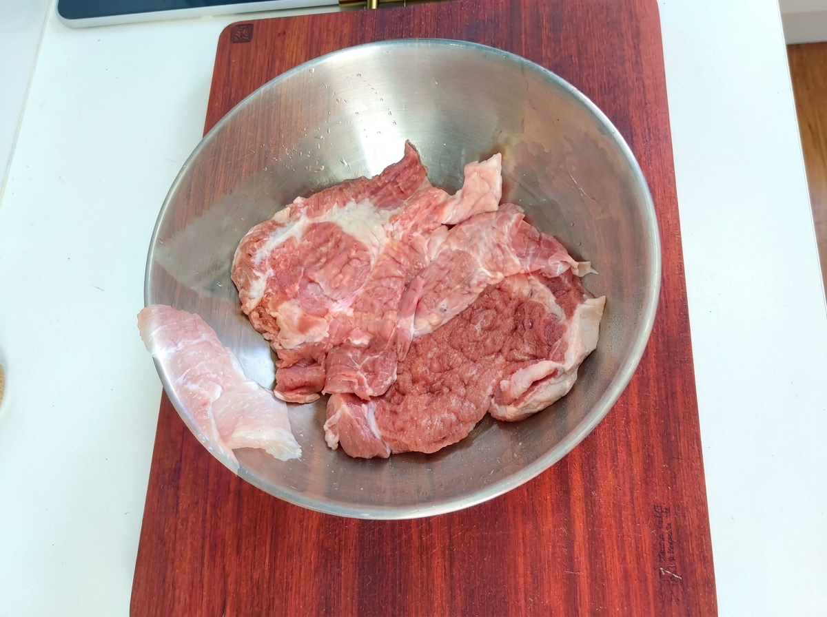 Pork pieces in a metal mixing bowl with marinade ingredients.