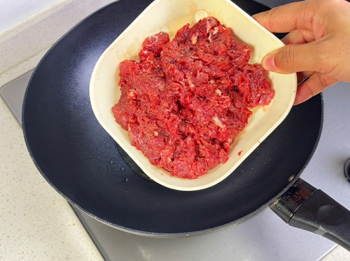Minced beef being added to a hot pan with oil to stir-fry.