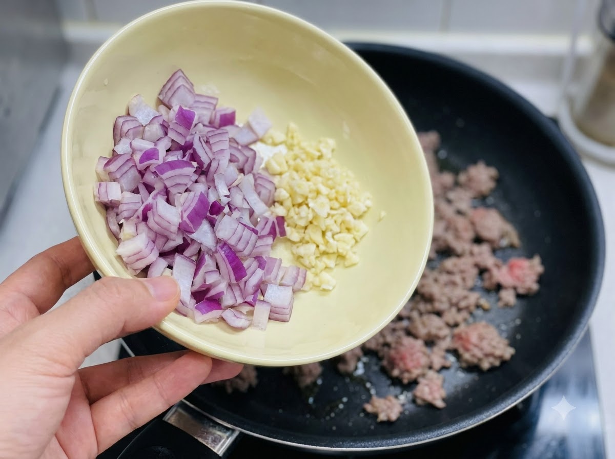 A bowl of chopped red onion and minced garlic being poured into the pan.