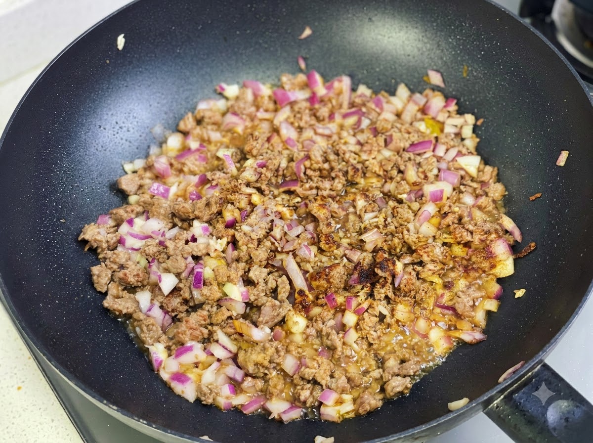 Curry paste and spices being sautéed with the beef and onion mixture in the pan.