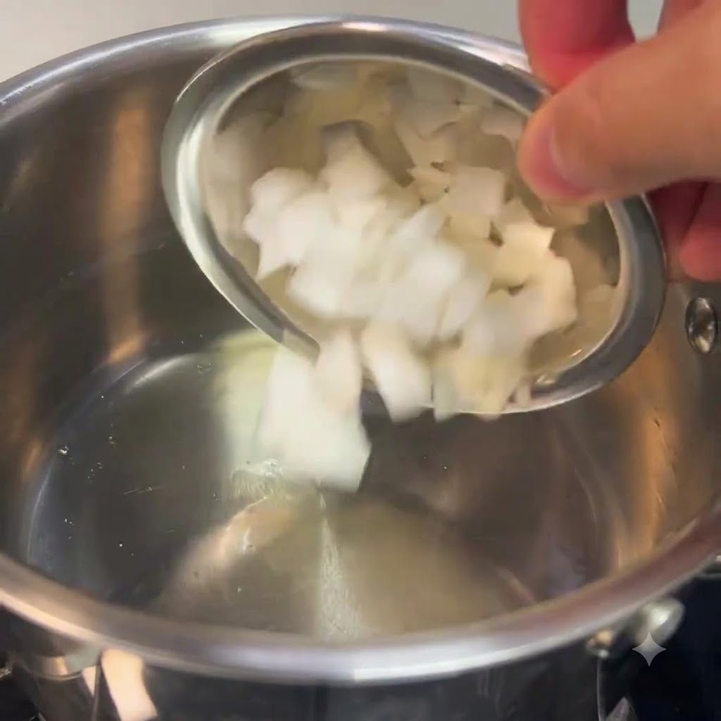 Chopped white onions being poured from a small bowl into a stainless steel pot.