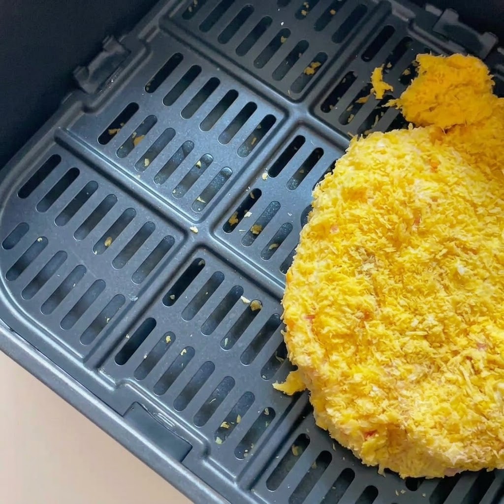 A breaded pork cutlet sitting inside a dark air fryer basket.
