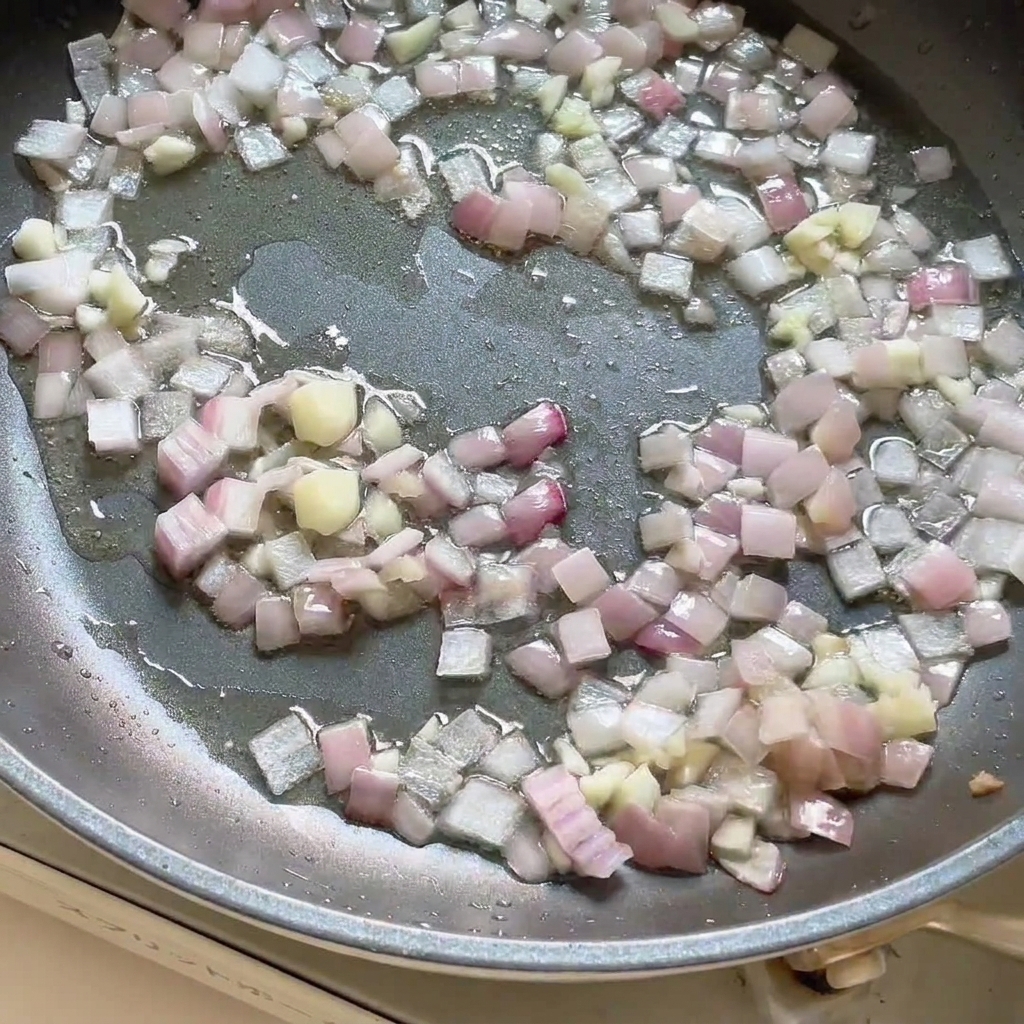 Curry paste added to the pan containing sautéed onions and garlic, being stirred together.