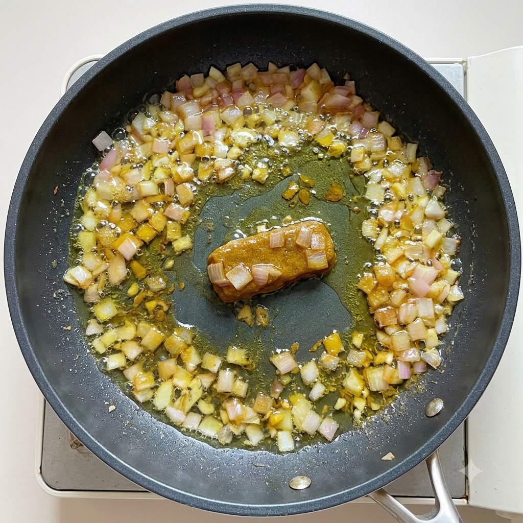 Water and coconut milk poured into the curry base in a frying pan, being stirred to a thick consistency.
