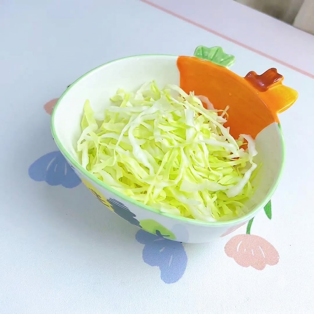 Shredded cabbage neatly arranged inside a decorative bowl with an orange carrot-shaped handle.