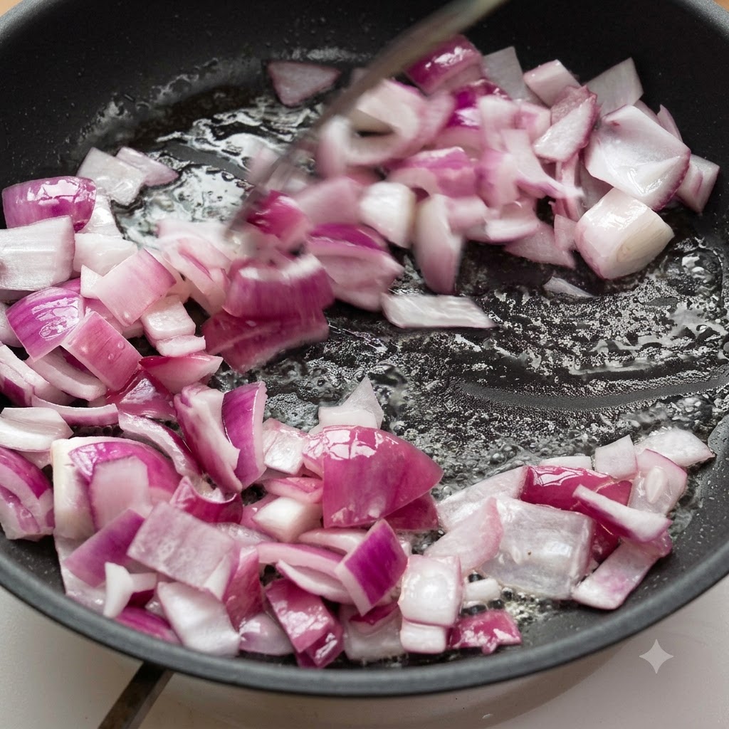 Chopped red onions being stir-fried in oil inside a frying pan.