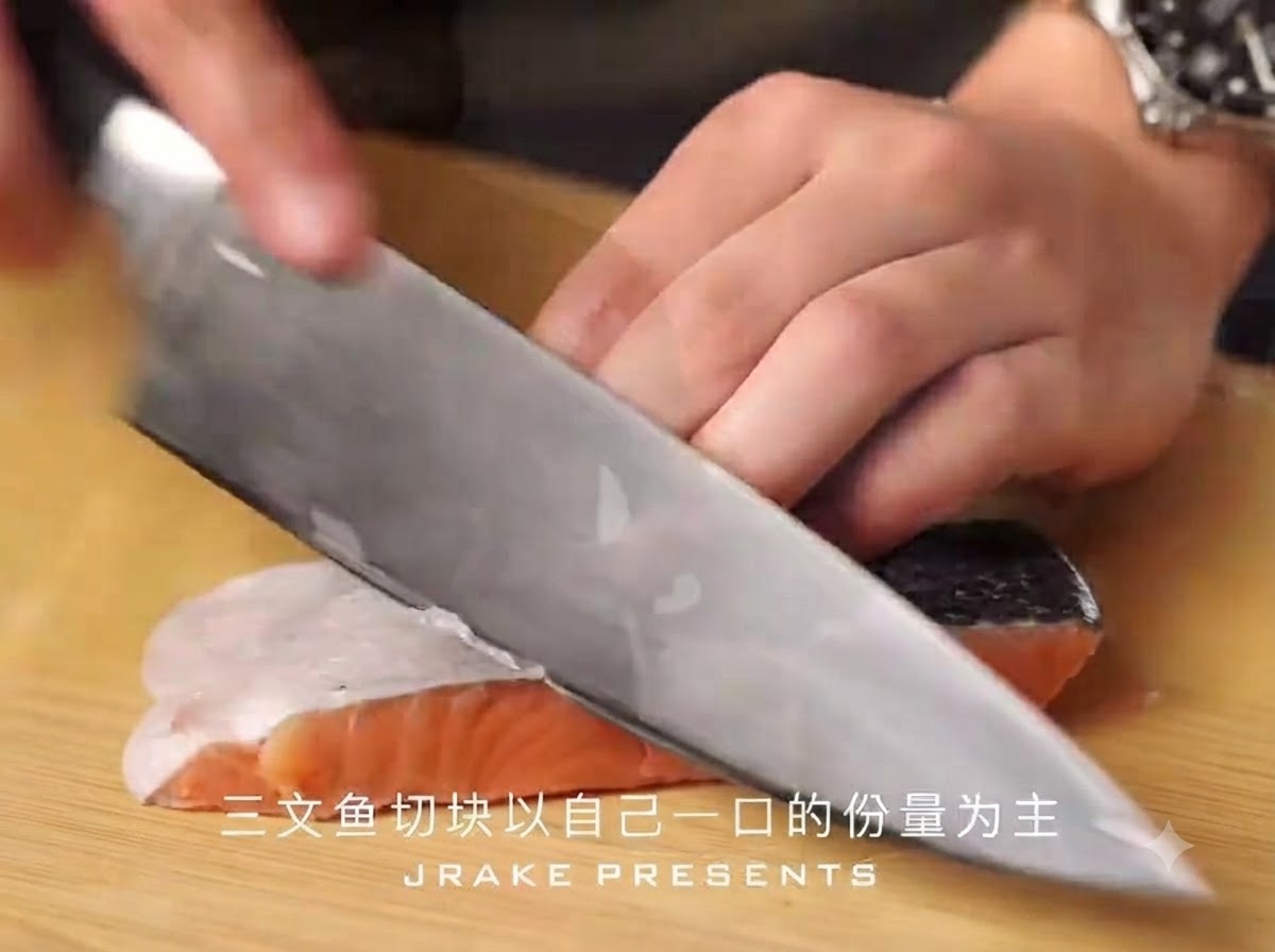 A sharp chefs knife slicing a salmon fillet with skin into bite-sized pieces on a wooden cutting board.