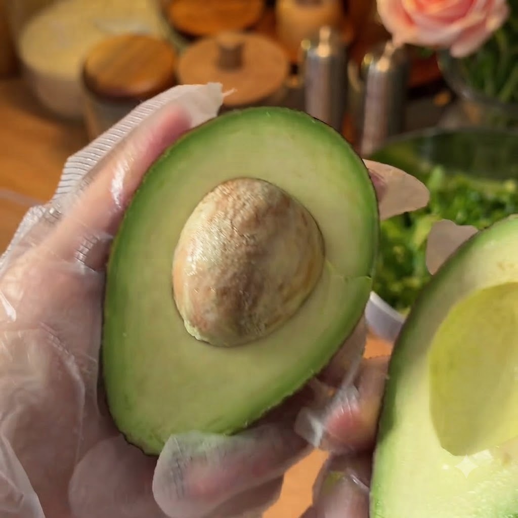 A halved fresh avocado being prepared on a cutting board.