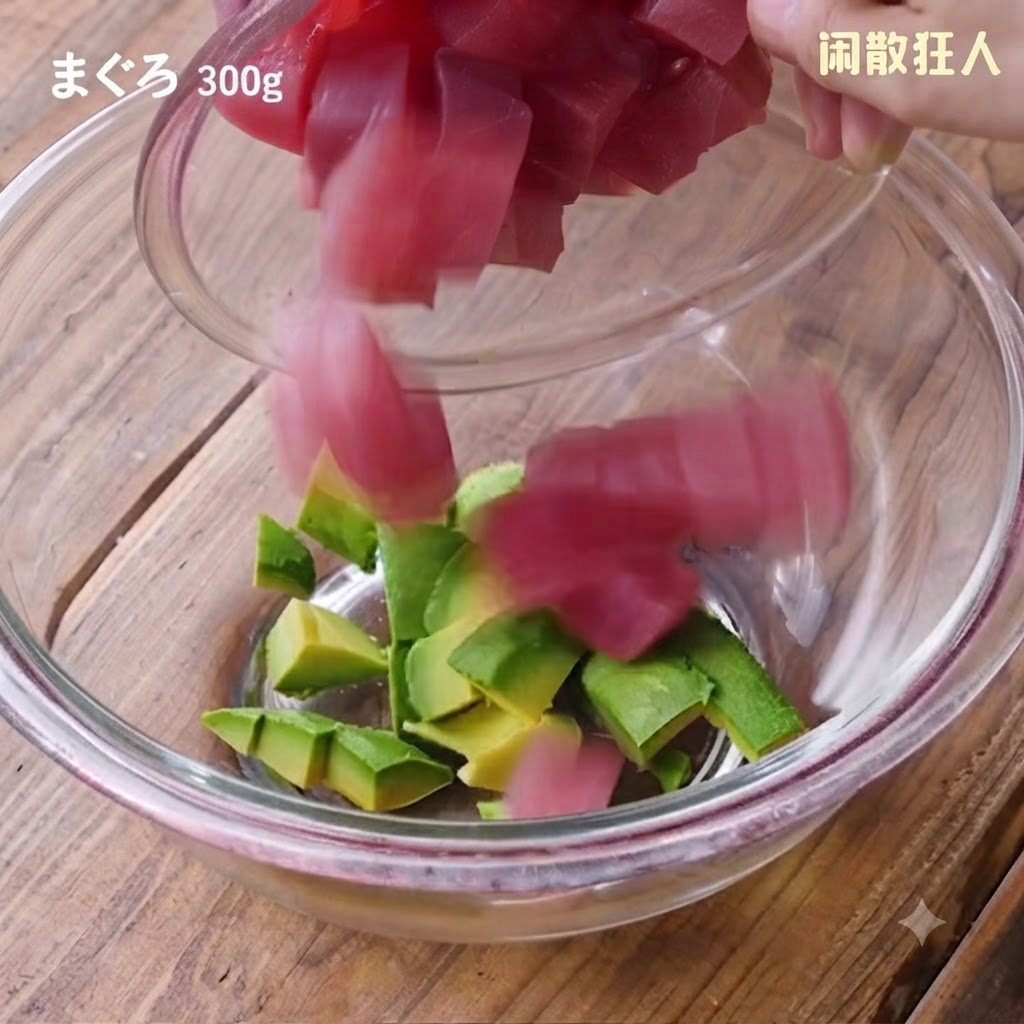Fresh cubed tuna pieces being poured from a small bowl into the glass bowl containing the avocado cubes.